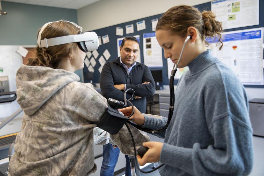 Student takes blood pressure of another student on stationary bike while faculty observes